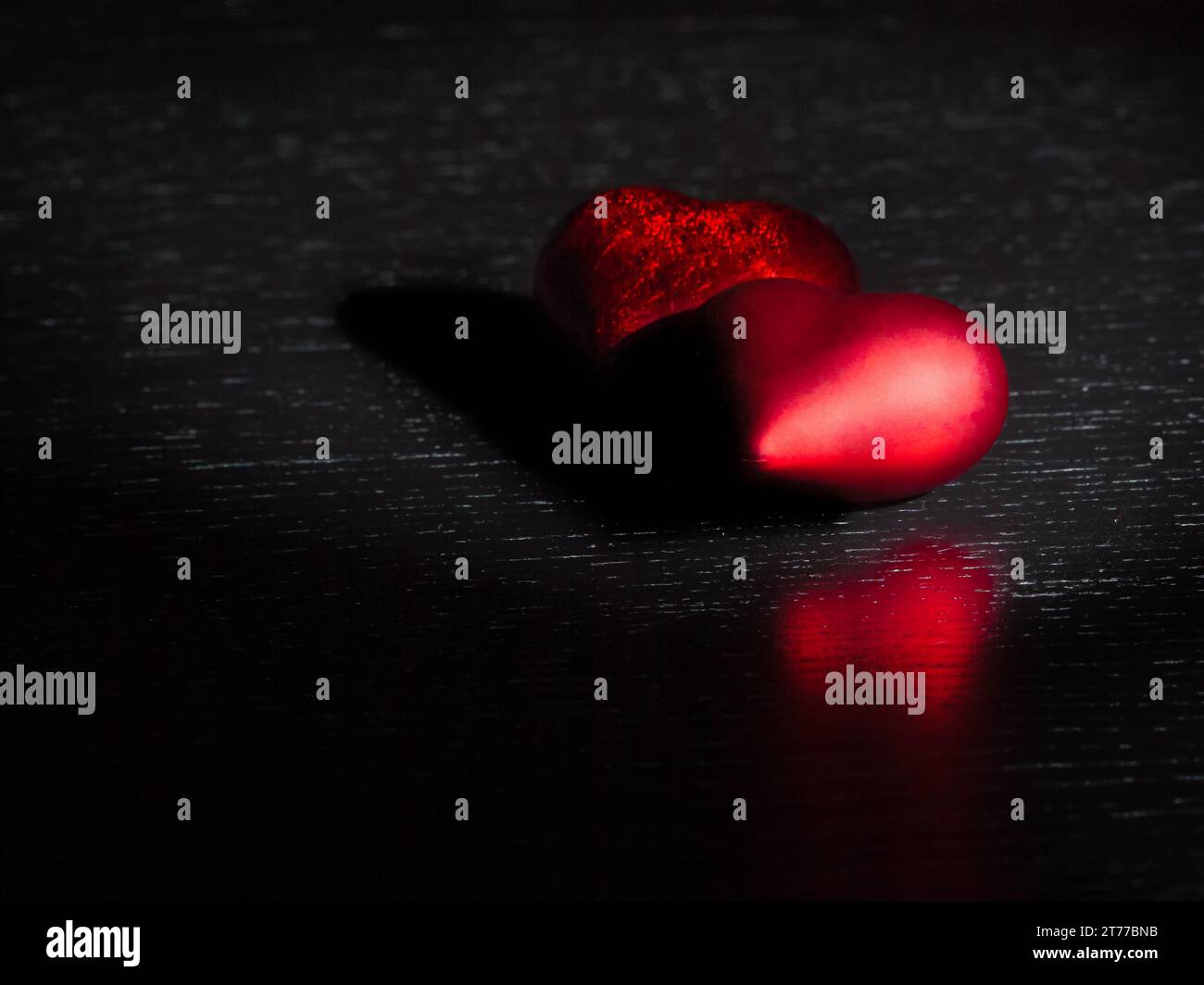 Zwei dekorative rote Herzen auf schwarzem Dunkellicht und auf Holztisch mit Platz für Text, Konzept des valentinstag Stockfoto