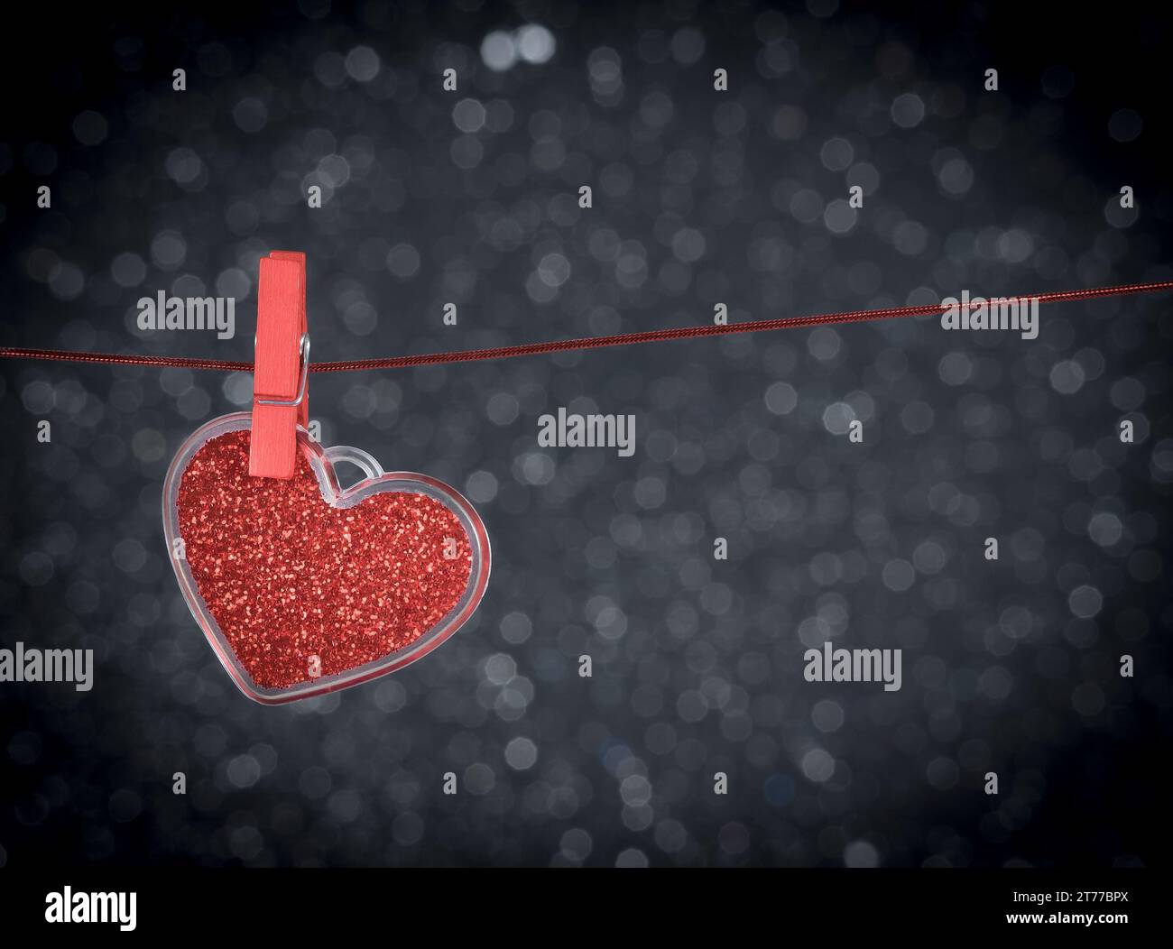 Dekoratives rotes Herz, das vor dunklem heller Bokeh-Hintergrund mit Platz für Text hängt, Konzept des valentinstages Stockfoto