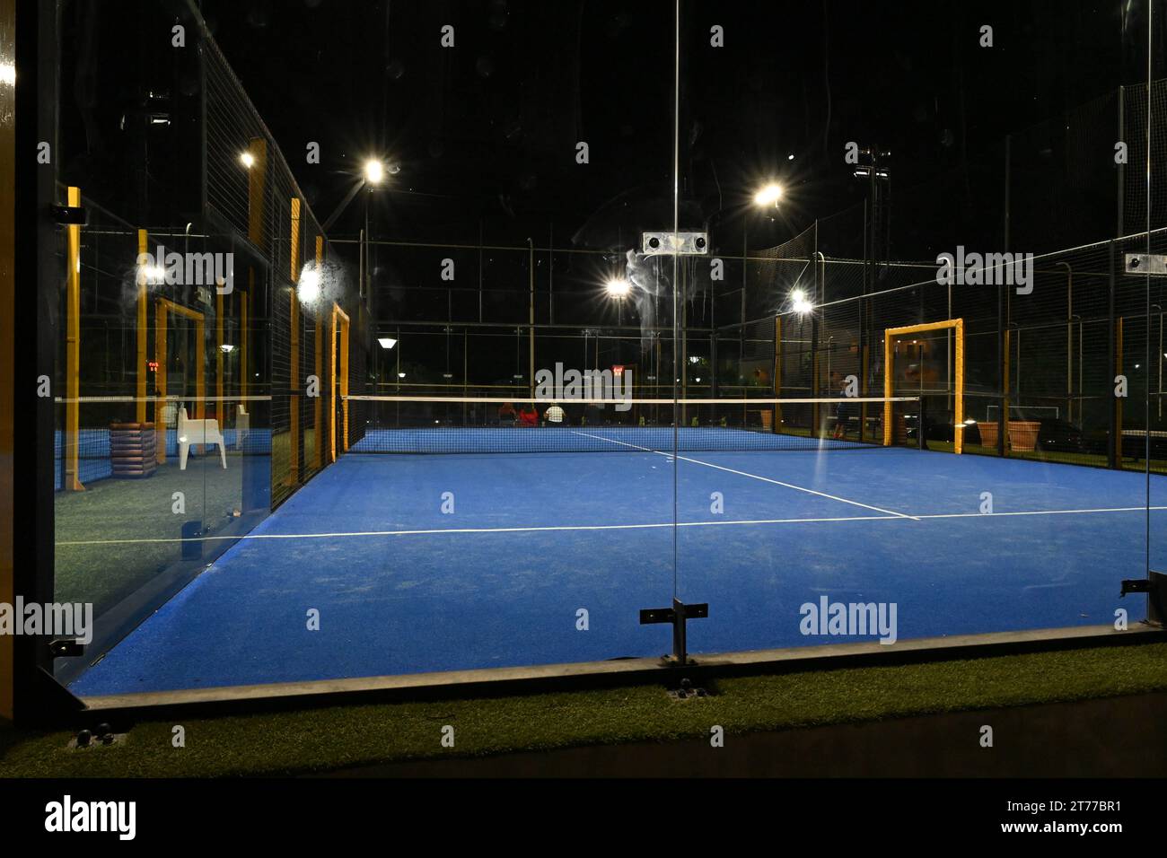Ein geschlossener blauer Platz für Padel in der Nacht mit Konstruktion aus Netz und Glasrückwänden. Stockfoto