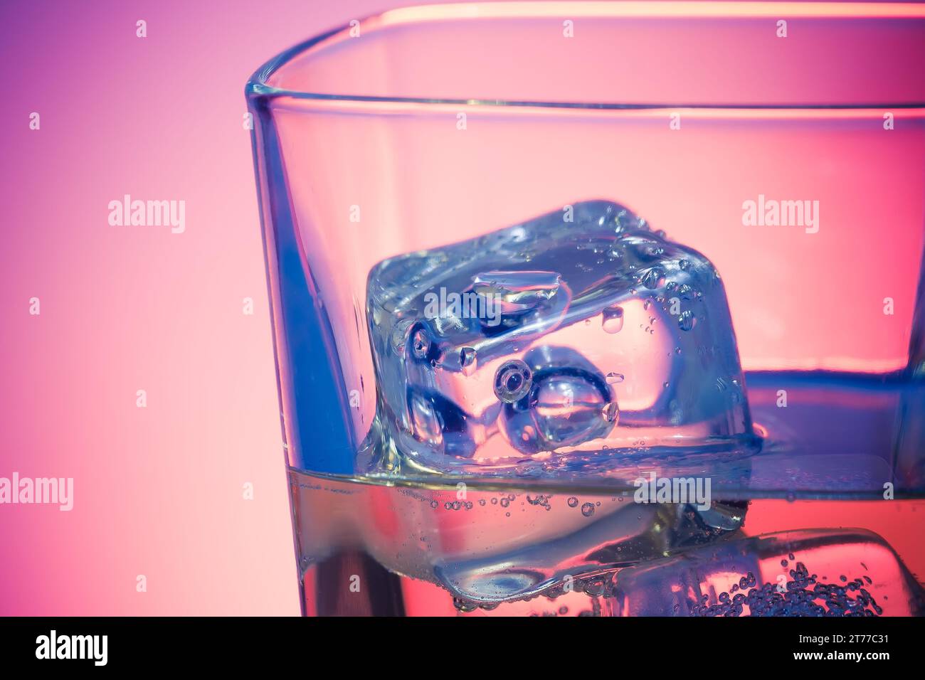 Glas alkoholisches Getränk mit Eis auf Disco violettem Licht auf weißem Tisch mit Platz für Text Stockfoto