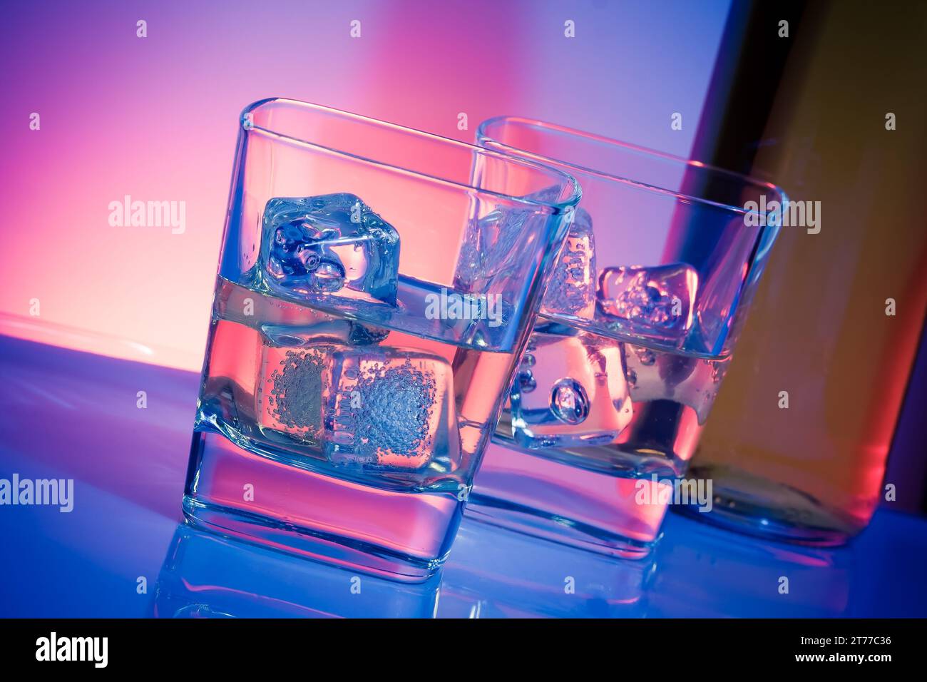 Ein paar Gläser alkoholischer Getränke mit Eis auf Disco-violettem Licht auf weißem Tisch Stockfoto
