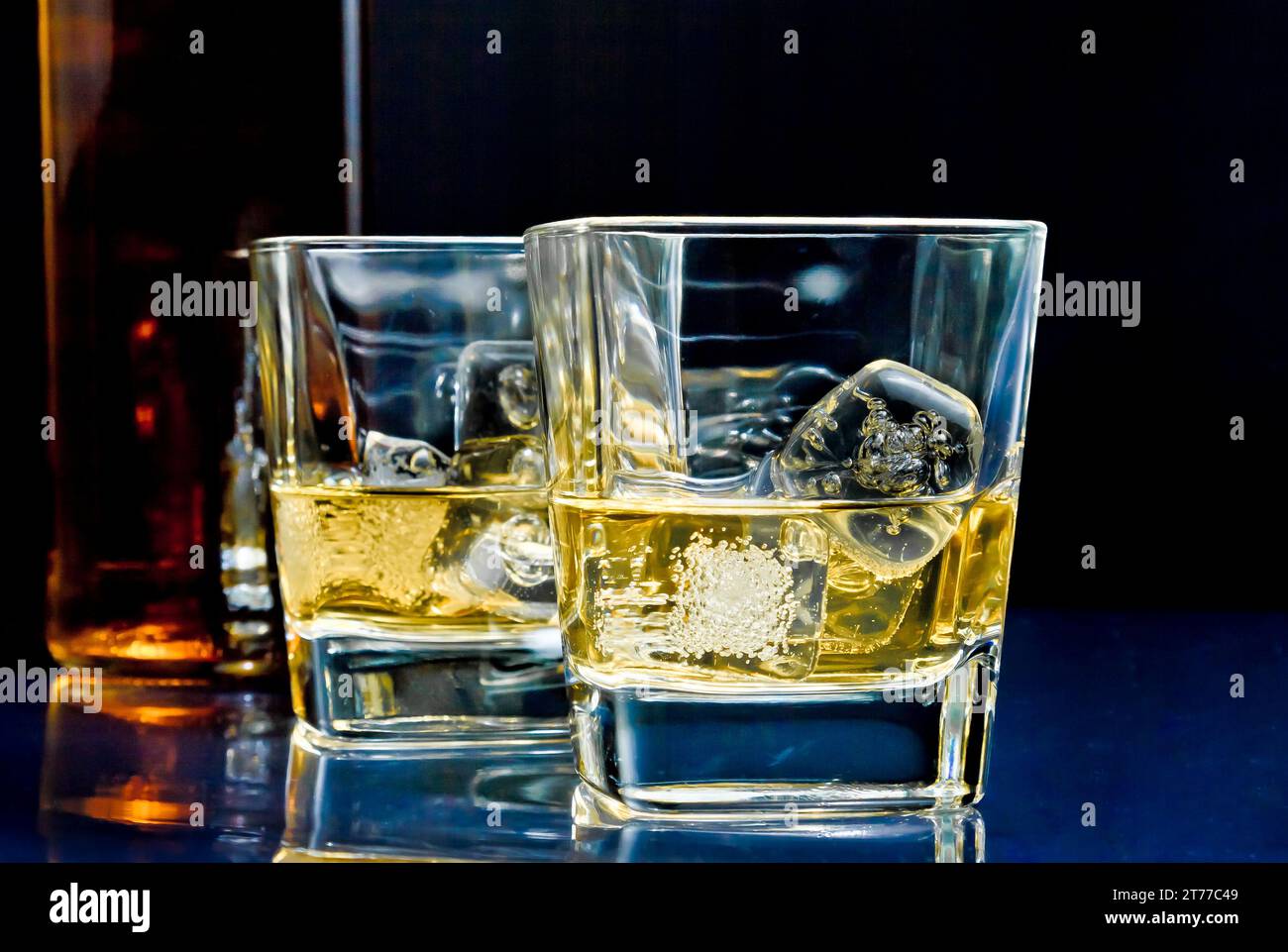 Zwei Gläser alkoholisches Getränk mit Eis auf Disco blauem Licht auf schwarzem Tisch Stockfoto