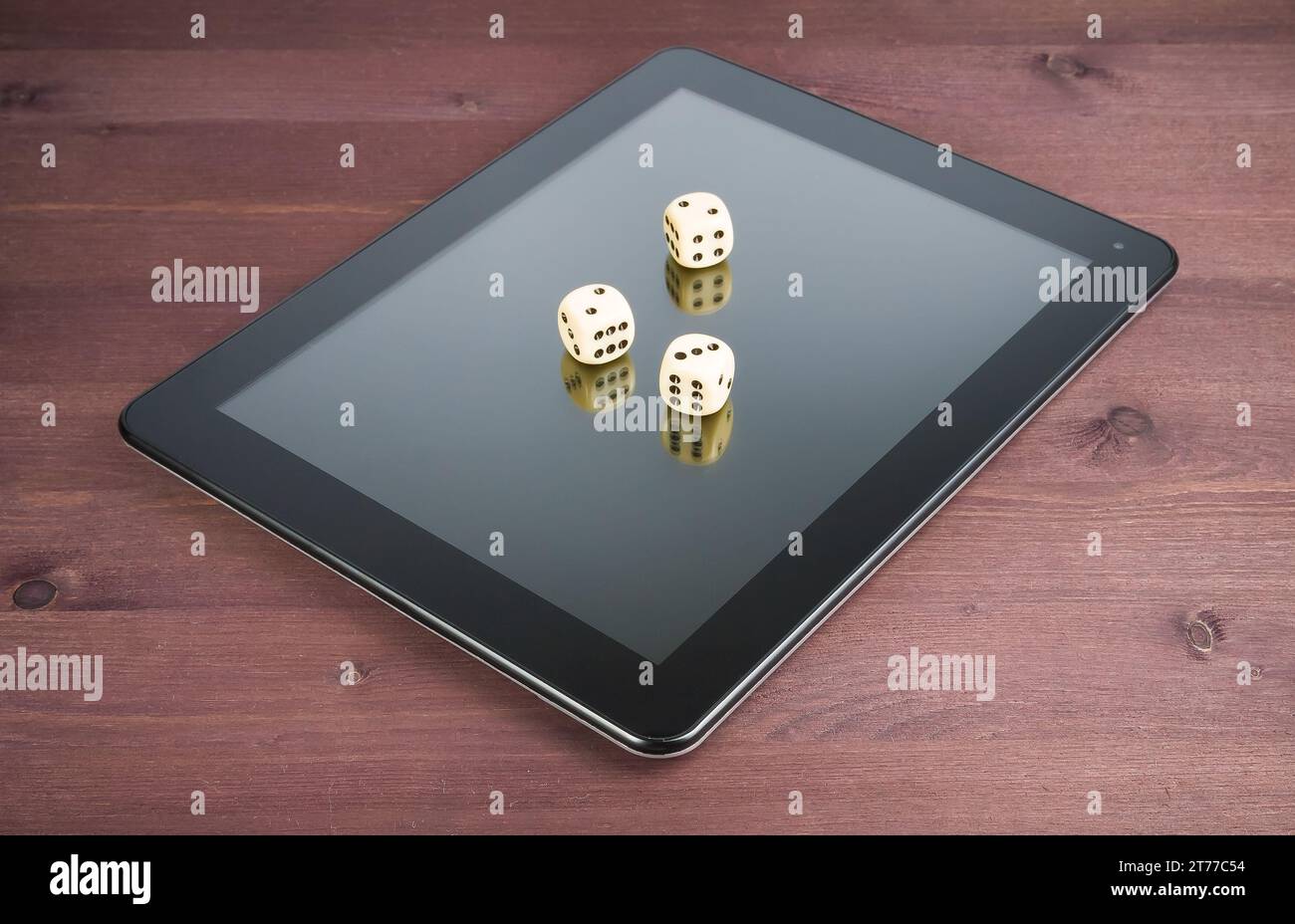 Drei Würfel auf einem digitalen Tablet-pc auf einem alten Holztisch, Konzept des texas-Spiels online Stockfoto