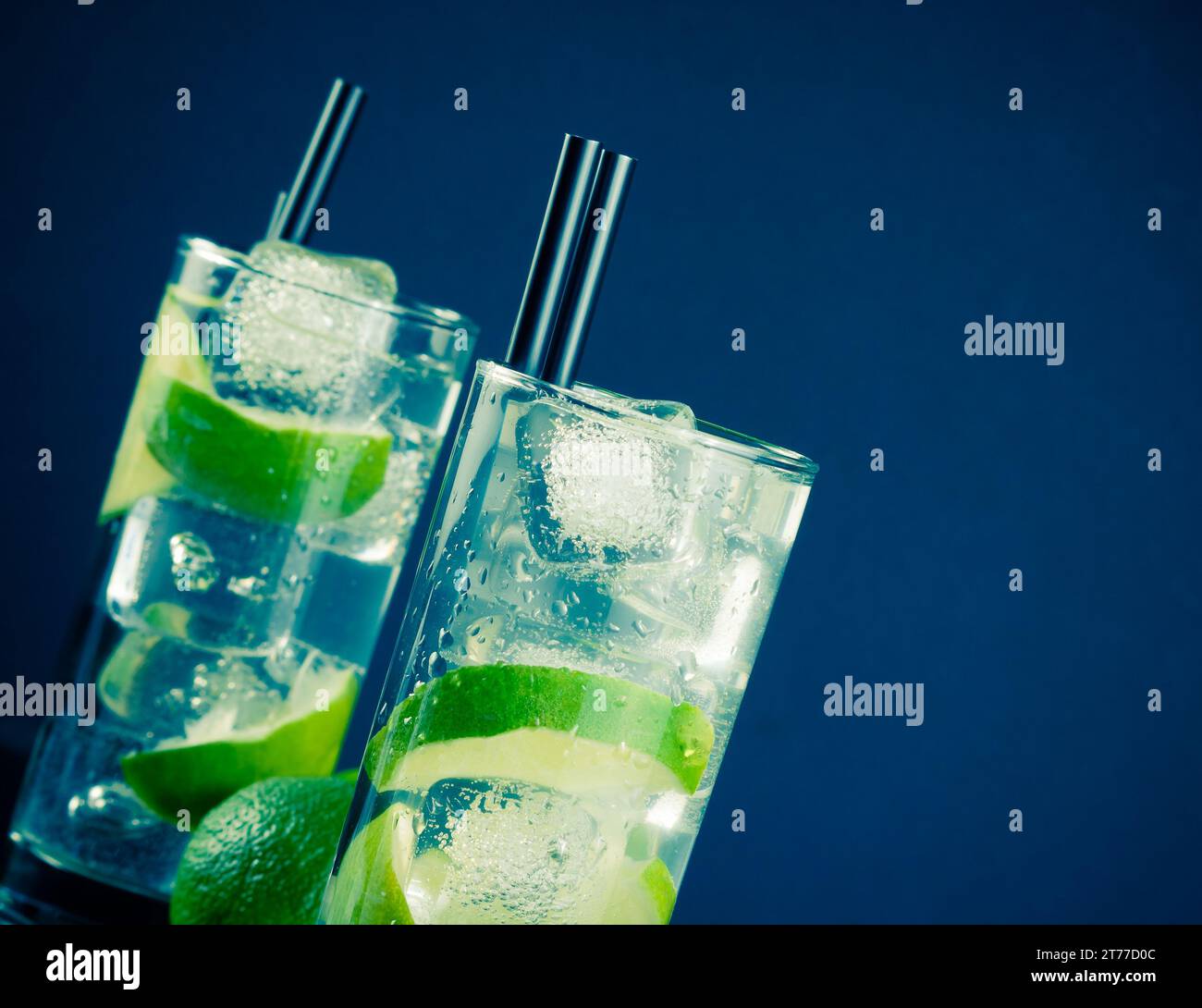 Zwei Gläser mit Cocktail und Eis mit Limettenscheibe in heller Disco-Atmosphäre Stockfoto