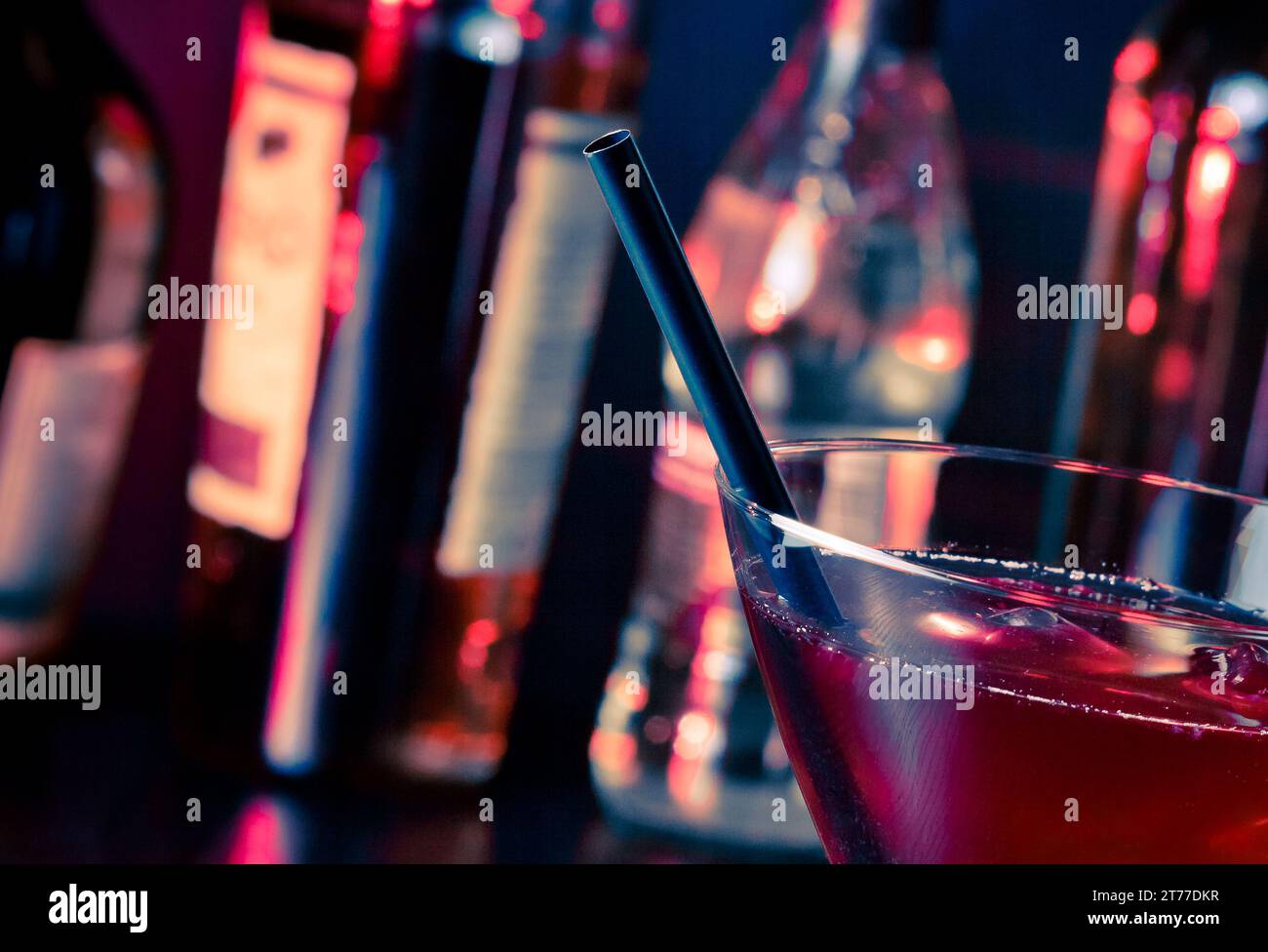 Detail eines roten Cocktails in einem Glas mit Eis und Platz für Text in heller Disco-Atmosphäre Stockfoto