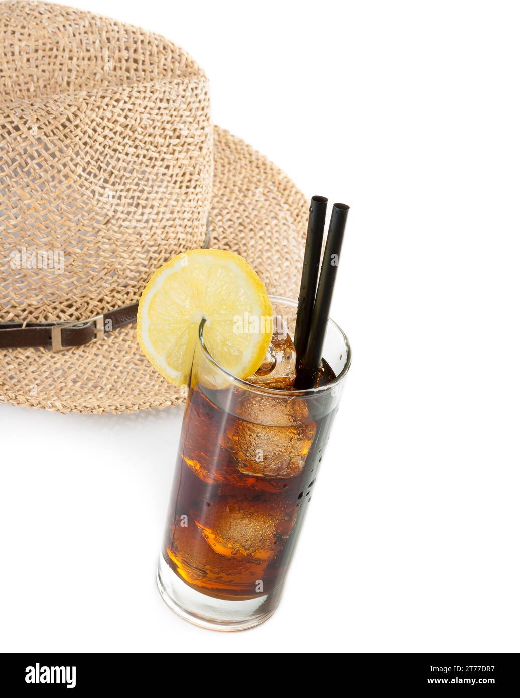 Glas frischer Cola mit Strohhalm vor dem Sommerhut auf weißem Hintergrund und Platz für Text, Sommerzeit Stockfoto
