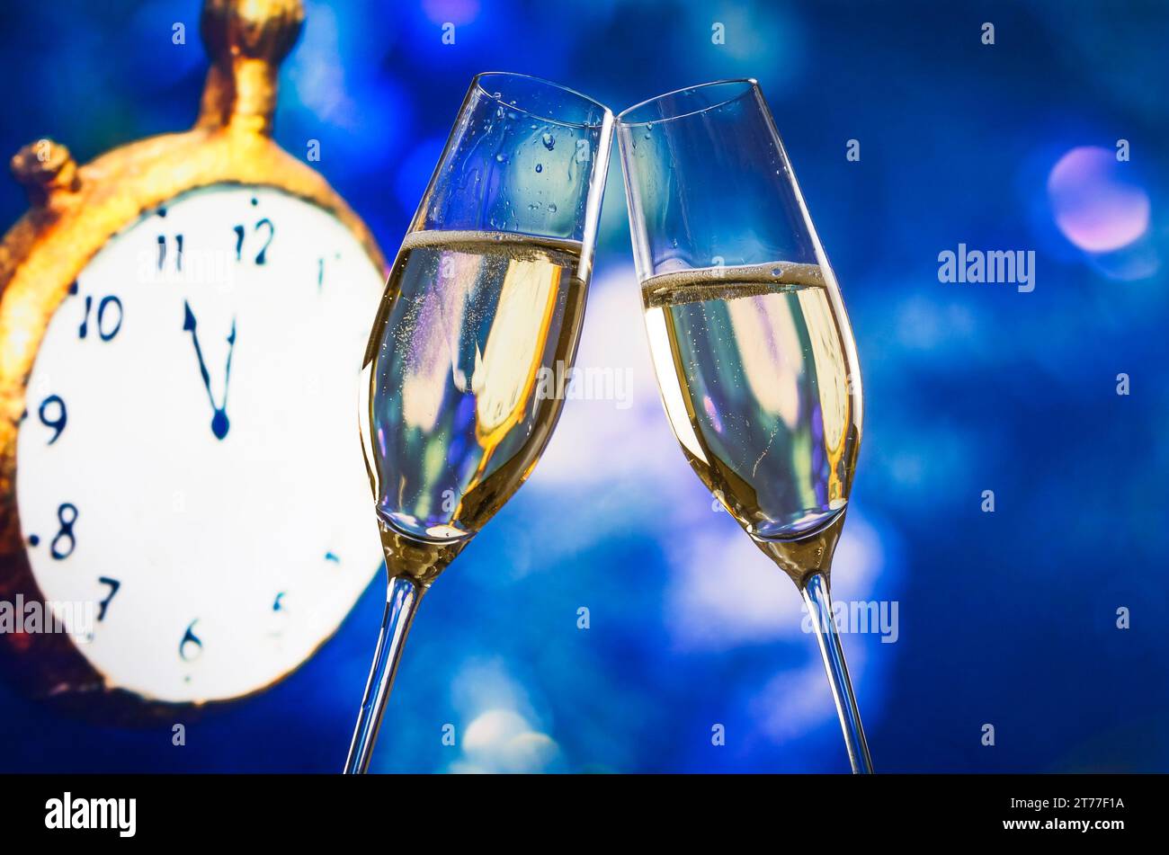 Silvester oder Weihnachten um Mitternacht mit Sektflöten machen Cheers Blue Bokeh und Uhr auf blauem Hintergrund Stockfoto