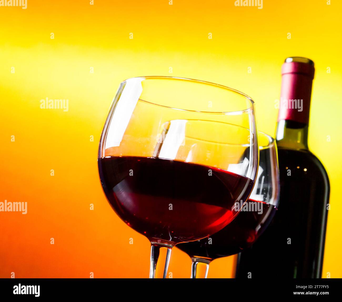 Zwei Rotweingläser neben der Flasche vor goldenem Hintergrund, festliches und unterhaltsames Konzept Stockfoto