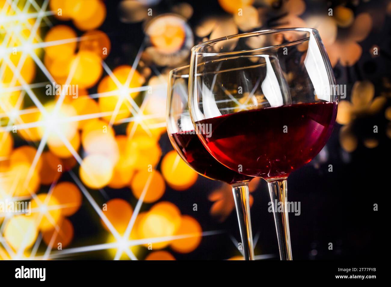 Zwei Rotweingläser vor goldenen Bokeh-Lichtern, festliches und unterhaltsames Konzept Stockfoto