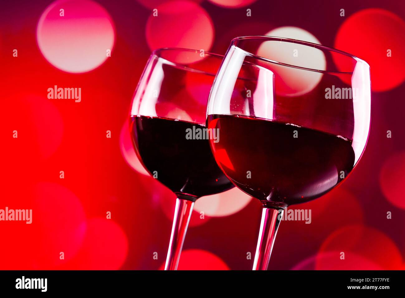 Zwei Rotweingläser vor rotem Bokeh-Hintergrund, festliches und unterhaltsames Konzept Stockfoto
