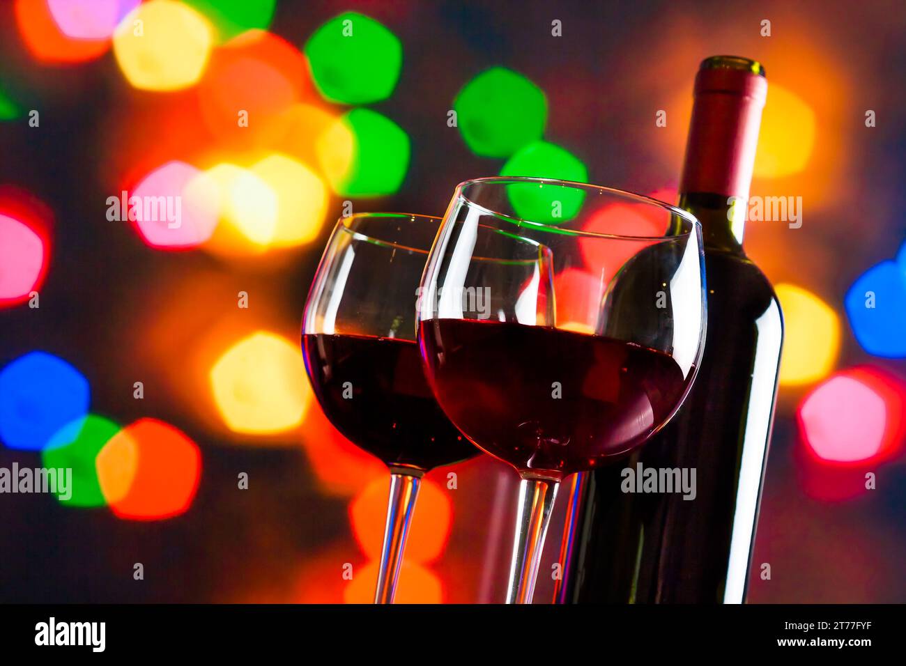 Zwei Rotweingläser in der Nähe der Flasche vor farbenfrohen Bokeh-Lichtern, festliches und unterhaltsames Konzept Stockfoto