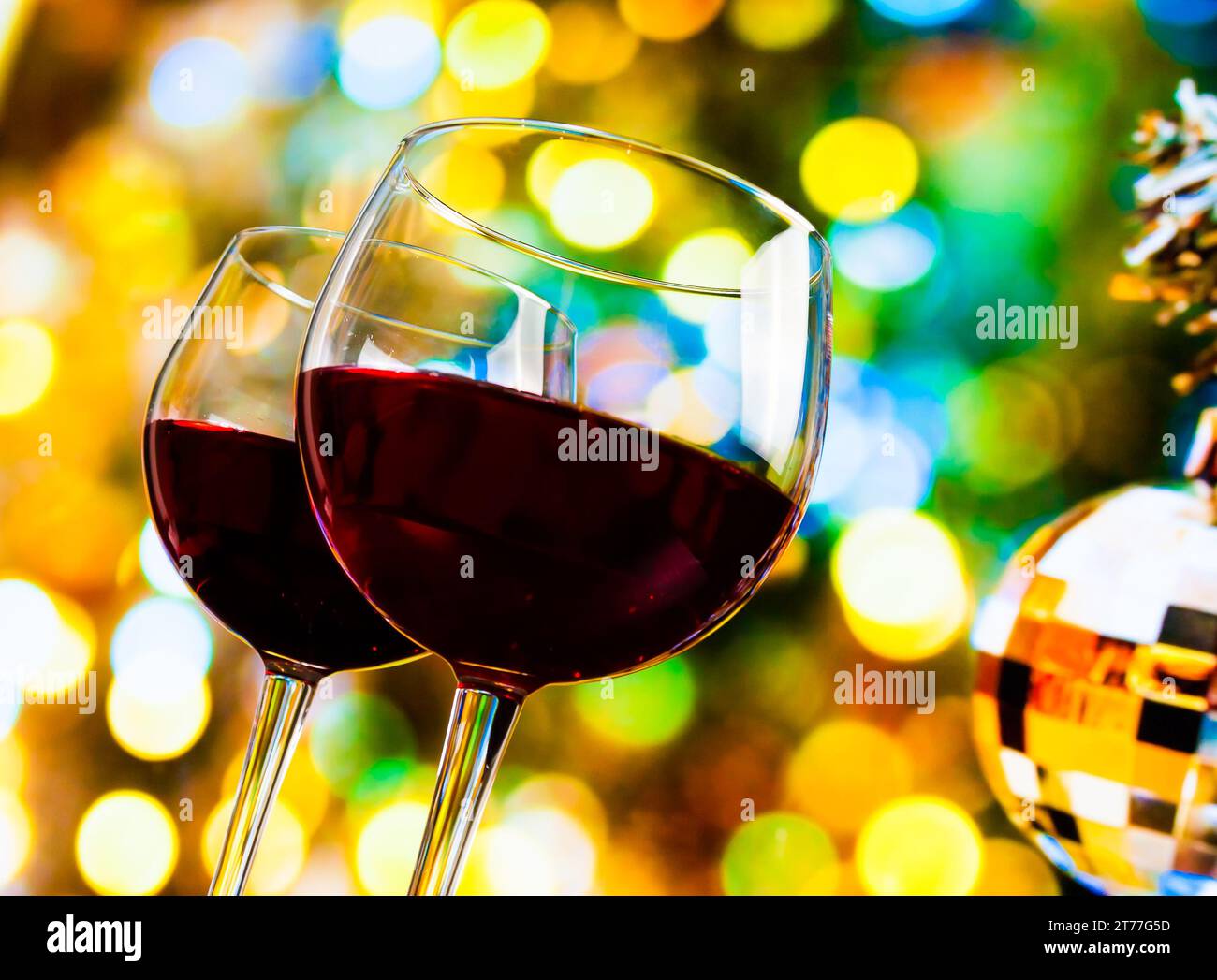 Zwei Rotweingläser vor bunten Bokeh-Lichtern und funkelndem Disco-Ball-Hintergrund, festliches und lustiges Konzept Stockfoto