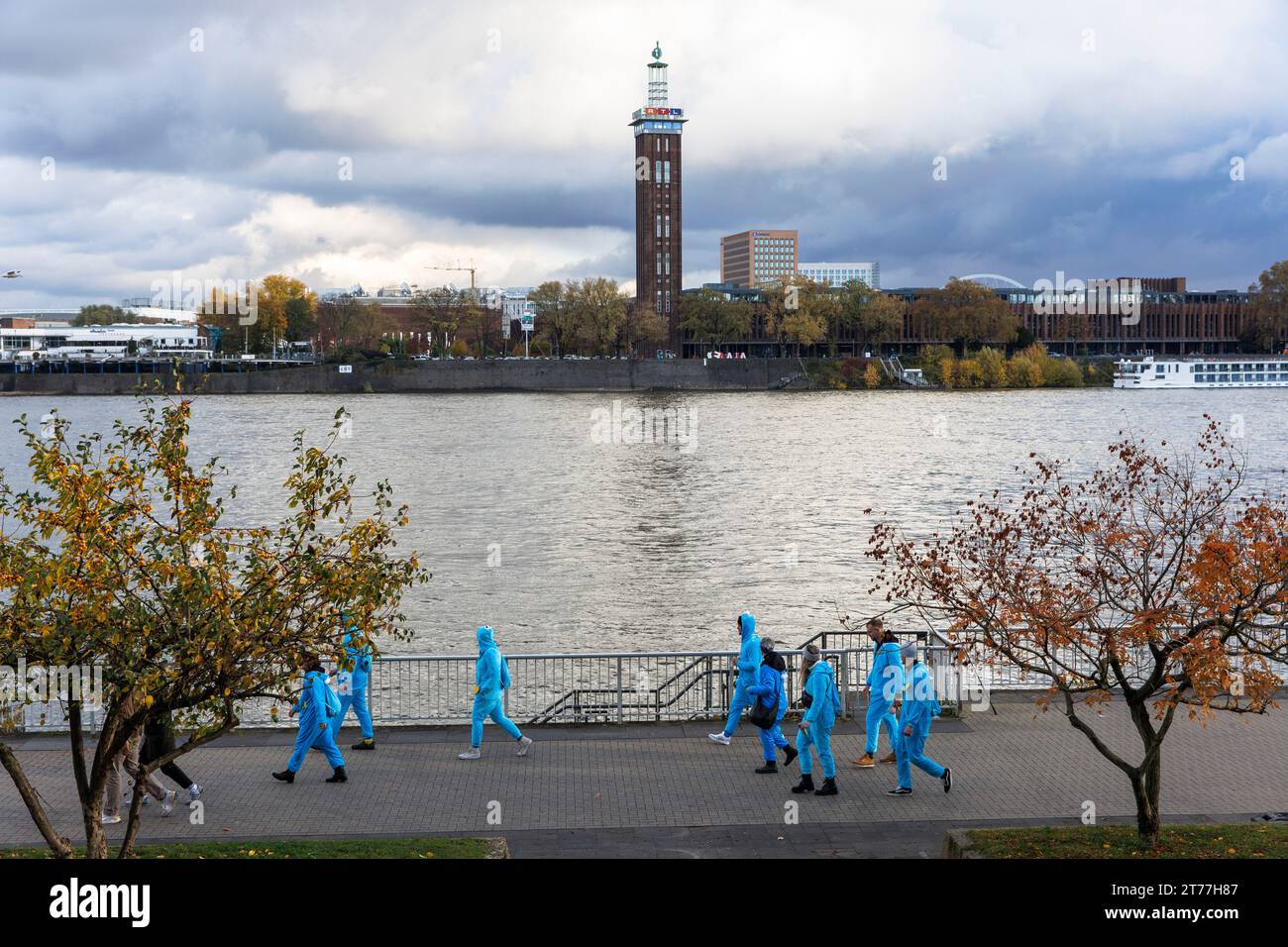 Am Tag der Eröffnung der Karnevalsveranstaltung am 11.11.23 spaziert eine Gruppe von Menschen in blauen Overalls am Ufer des Rheins entlang, dem alten Turm des f Stockfoto
