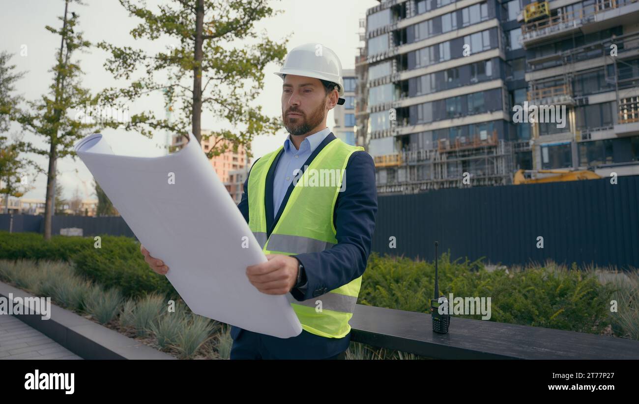 Kaukasischer lächelnder erwachsener Mann in der Stadt mit Blueprint Papier Dokument Plan Arbeit im Freien männlicher Architekt Guy prüft städtische Gebäude Architektur Geschäft Stockfoto