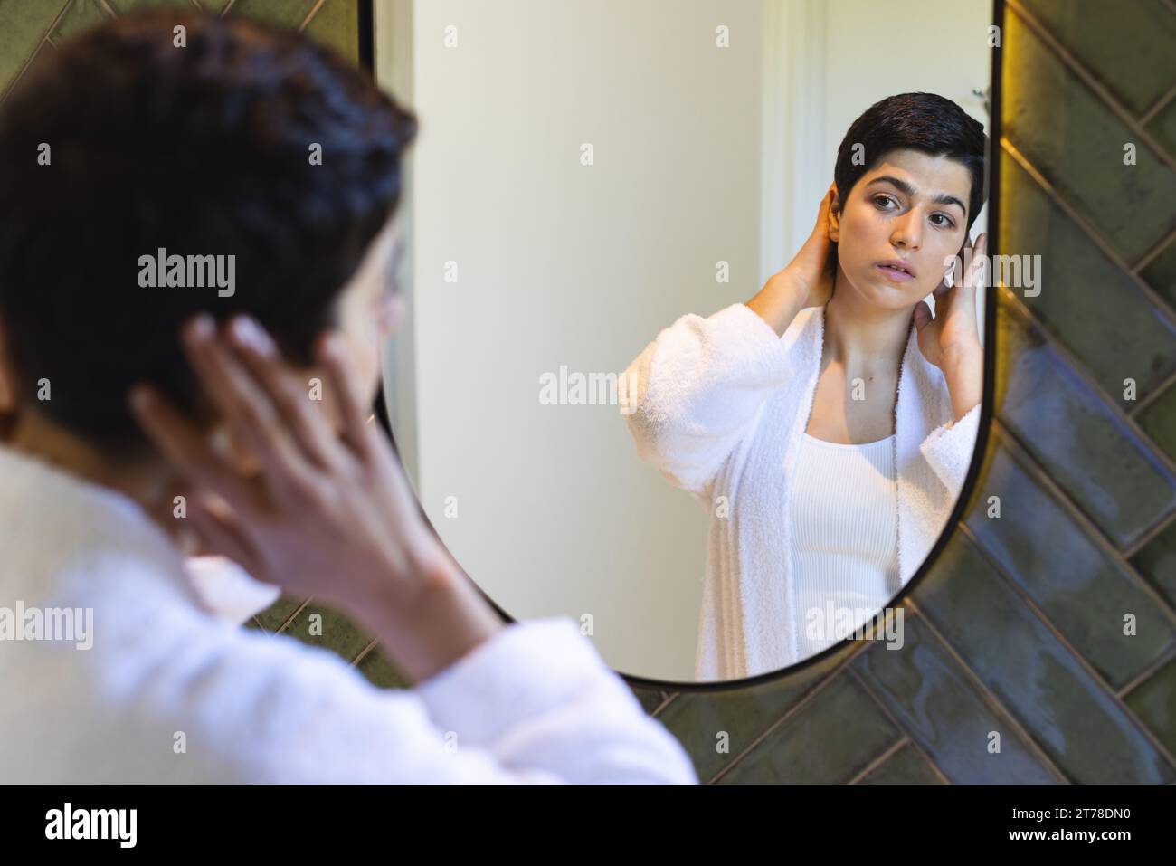 Glückliche birassische Frau, die Haare berührt und zu Hause im Badezimmerspiegel reflektiert Stockfoto