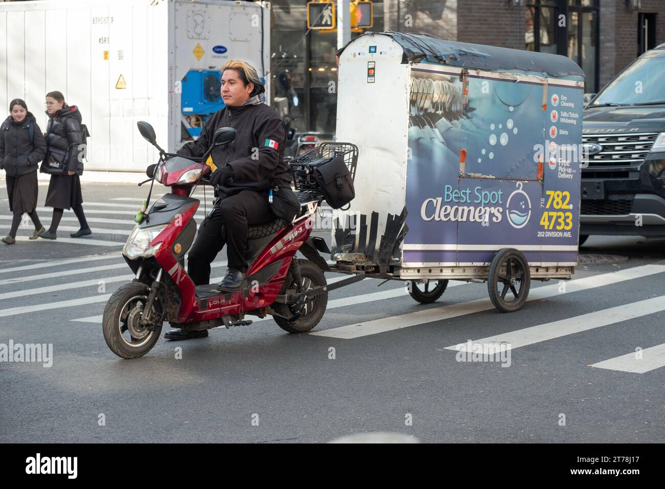 Ein Liefermann mit mexikanischer Flagge auf dem Mantel liefert Kleidung von Best Spot Cleaners in einem Trailer, um zu vermeiden, dass die Kleidungsstücke zerknittert werden. In NYC. Stockfoto
