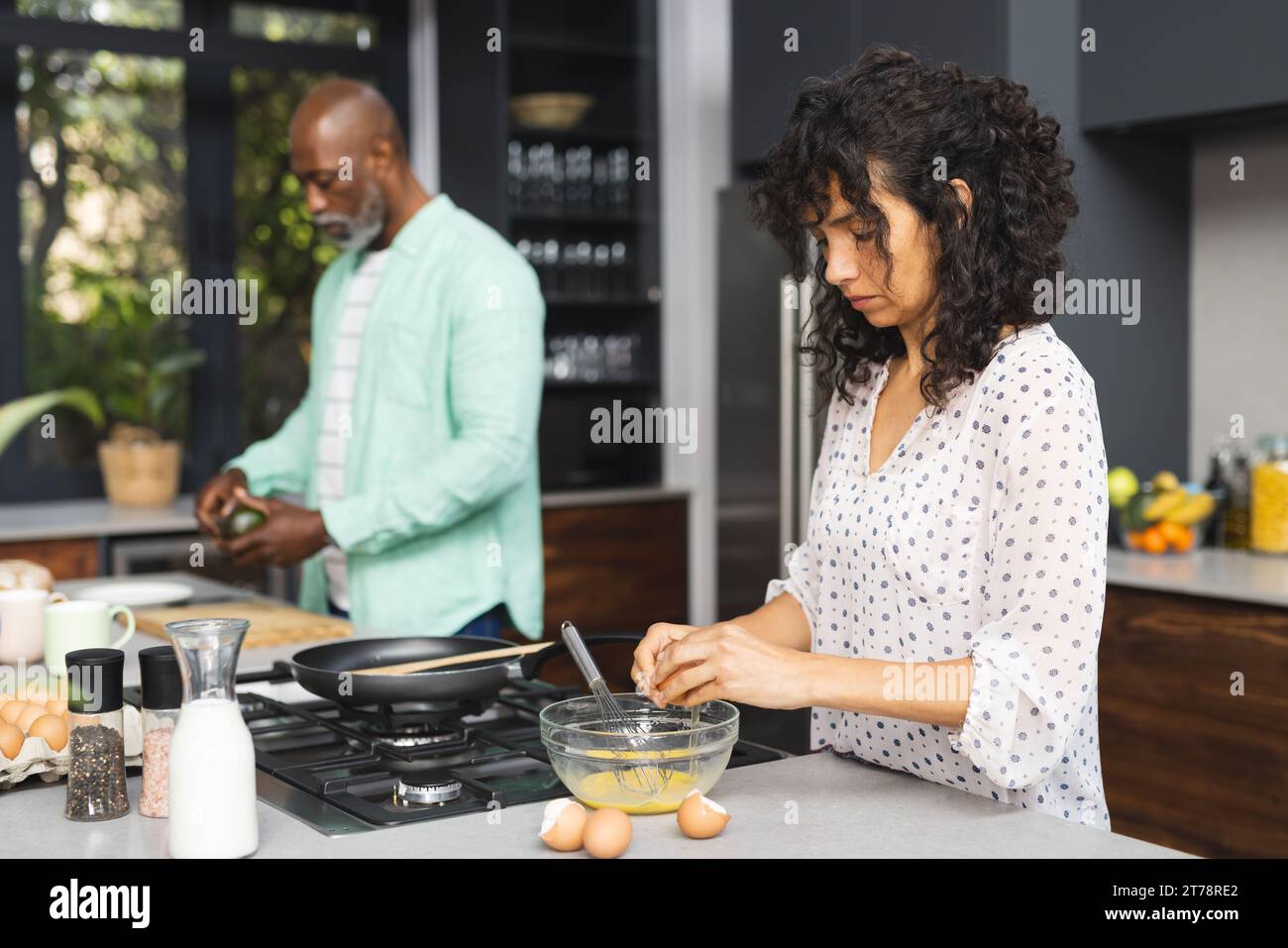 Fokussiertes reifes, vielfältiges Paar, das Eier bricht und Frühstück in der sonnigen Küche zubereitet Stockfoto