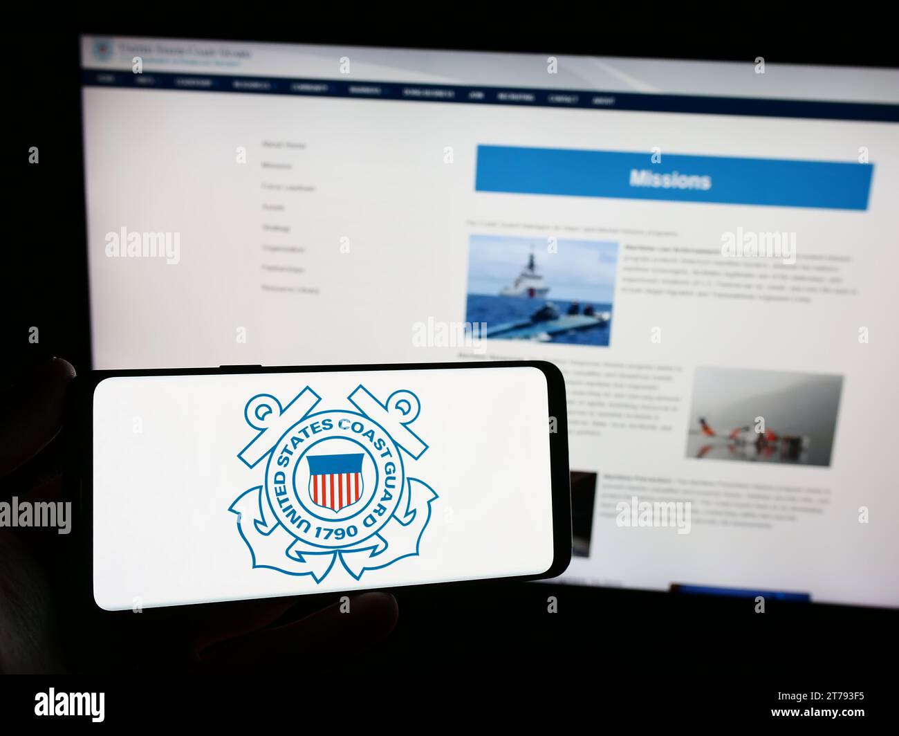 Person, die ein Smartphone mit dem Siegel der United States Coast Guard (USCG) vor der Website hält. Schwerpunkt auf dem Display des Telefons. Stockfoto