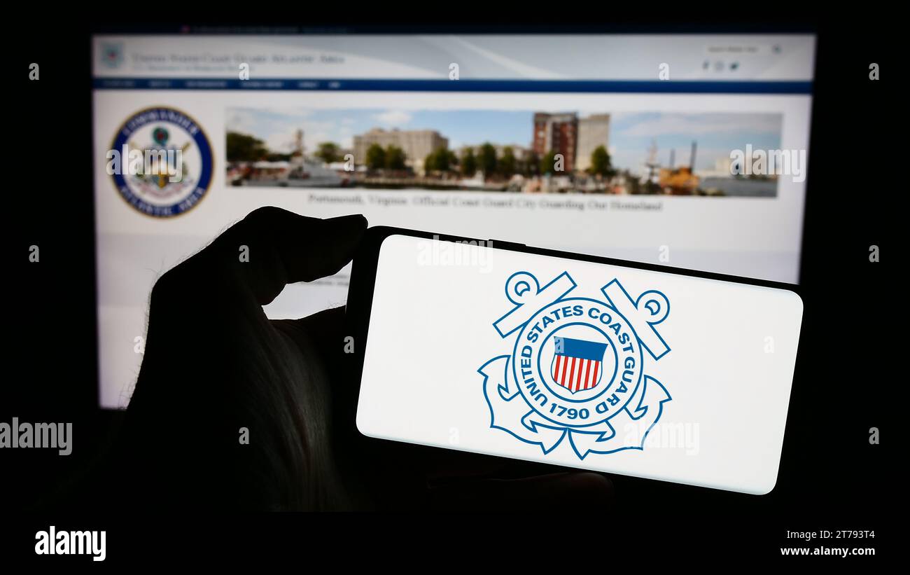 Person, die ein Mobiltelefon mit dem Siegel der United States Coast Guard (USCG) vor der Webseite hält. Schwerpunkt auf dem Display des Telefons. Stockfoto