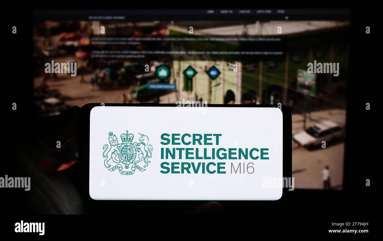 Person mit Handy und Siegel der britischen Agentur Secret Intelligence Service (SIS, MI6) vor der Webseite. Schwerpunkt auf dem Display des Telefons. Stockfoto