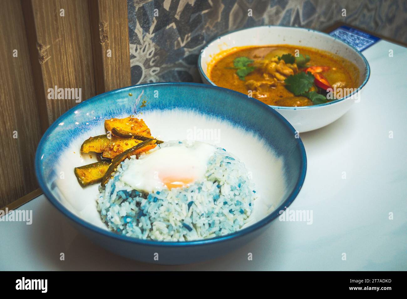 Eine Schüssel Curry-Huhn mit Kartoffeln und Butterfly-Erbsenreis und eingelegtem Achar und Spiegelei Stockfoto