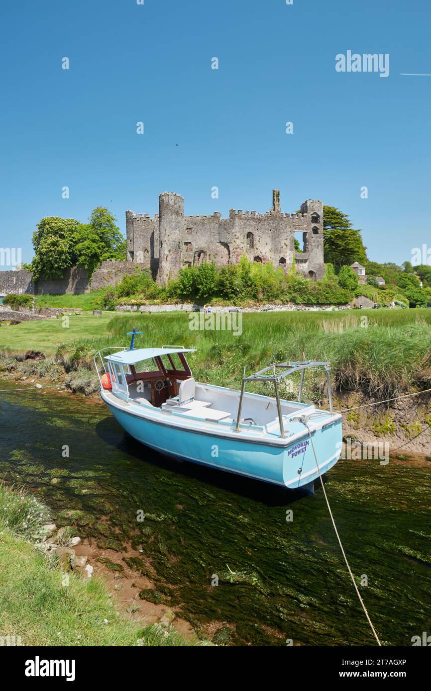 Laugharne Castle, mit einem kleinen Fischerboot auf dem Fluss Coran, Wales, Großbritannien Stockfoto