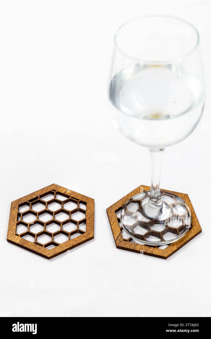Sammlung von hölzernen Untersetzern mit komplizierten Designs und einem Weinglas auf weißem Hintergrund. Die Untersetzer sind sechseckig. Stockfoto