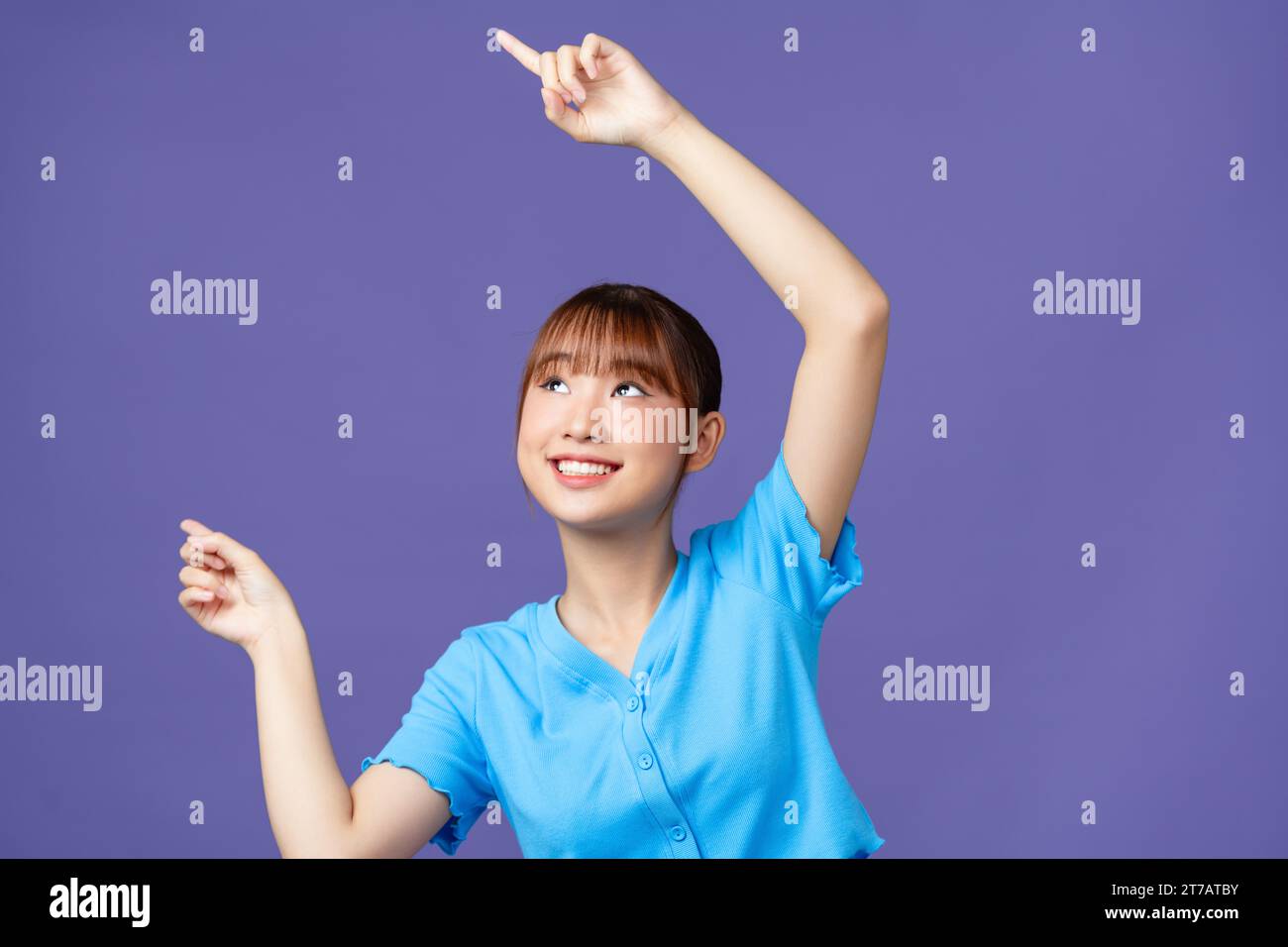 Fühlen Sie die Freude mit einer jungen asiatischen Frau, die auf freien Kopierraum auf violettem Hintergrund zeigt Stockfoto