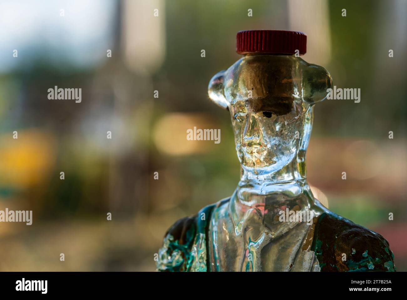 Eine skurrile Glasflasche, die in Form eines Mannes mit Korkhut gefertigt wurde, steht vor dem Hintergrund eines lebendigen bunten Bokeh und schafft ein Playfu Stockfoto