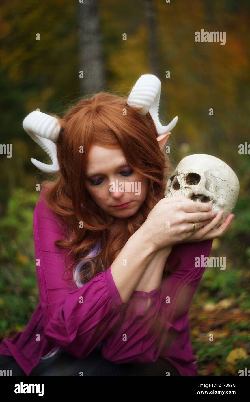 Eine ergreifende Szene mit einem Tiefling von Dungeons & Dragons, der einen Schädel hält und traurig auf den Boden blickt. Auffällige Details, lila Bluse, Stockfoto