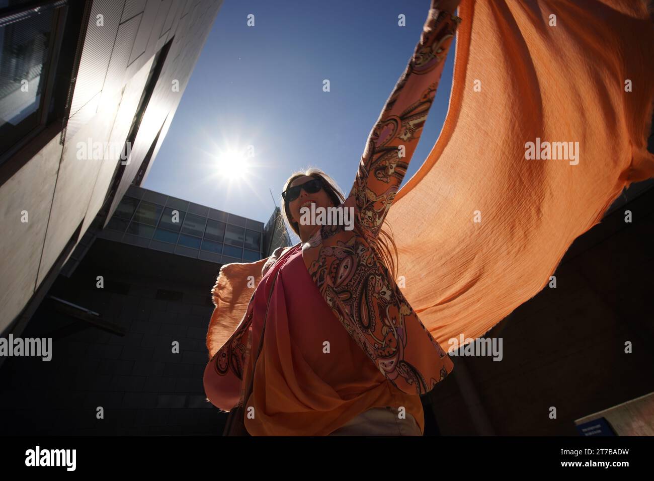 Erfolgreiche positive Frau in orangefarbenen Modekleidern, die einen orangefarbenen Schal winkt Stockfoto