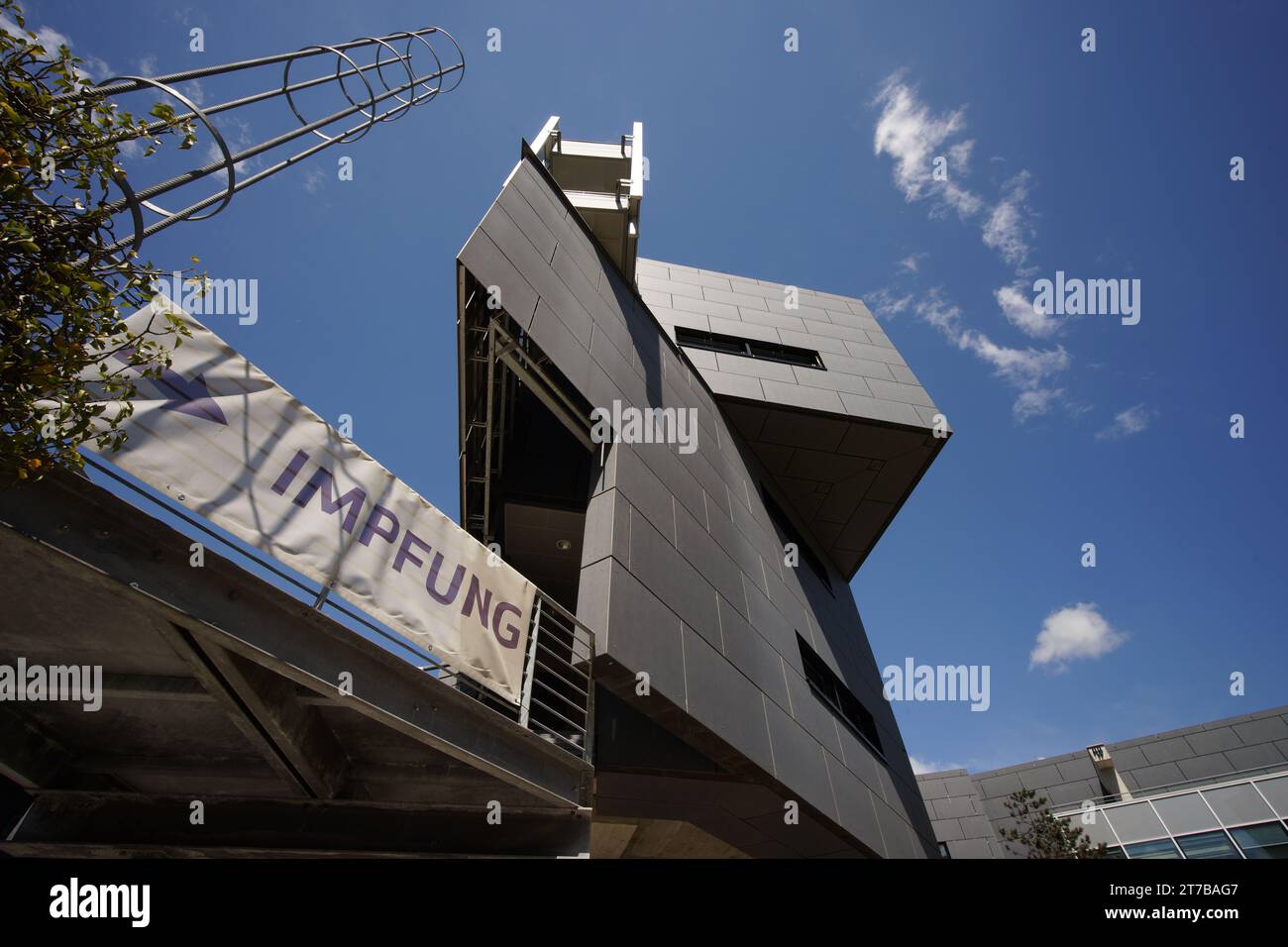 Modernes Gebäude mit dreieckiger Fassade und Wegpunktschild mit deutschem Wort Impfung, englisch: Impfung Stockfoto Modernes Gebäude mit dreieckiger Fassade und Wegpunktschild mit deutschem Wort Impfung, englisch: Impfung Stockfoto