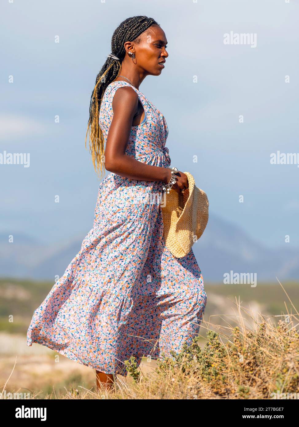 Ganzkörperporträt einer ausdrucksstarken jungen Afrikanerin in einem traumhaften Kleid mit Hut und Blick auf den Atlantischen Ozean. Stockfoto