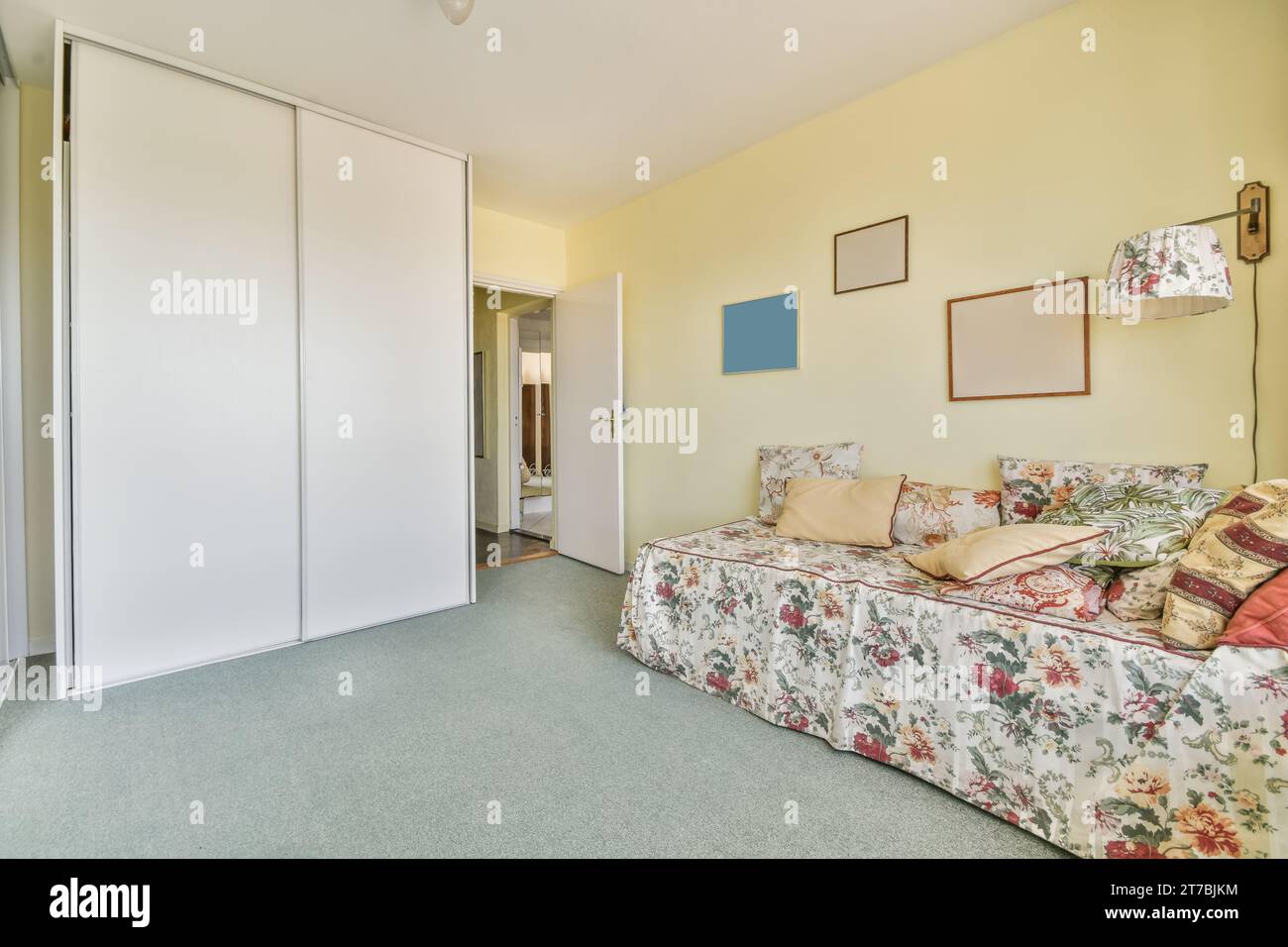 Ein Wohnzimmer mit gelben Wänden und geblümtem Bett, das über das Zimmer verteilt ist, es gibt eine offene Tür, die zu einem anderen Zimmer führt Stockfoto