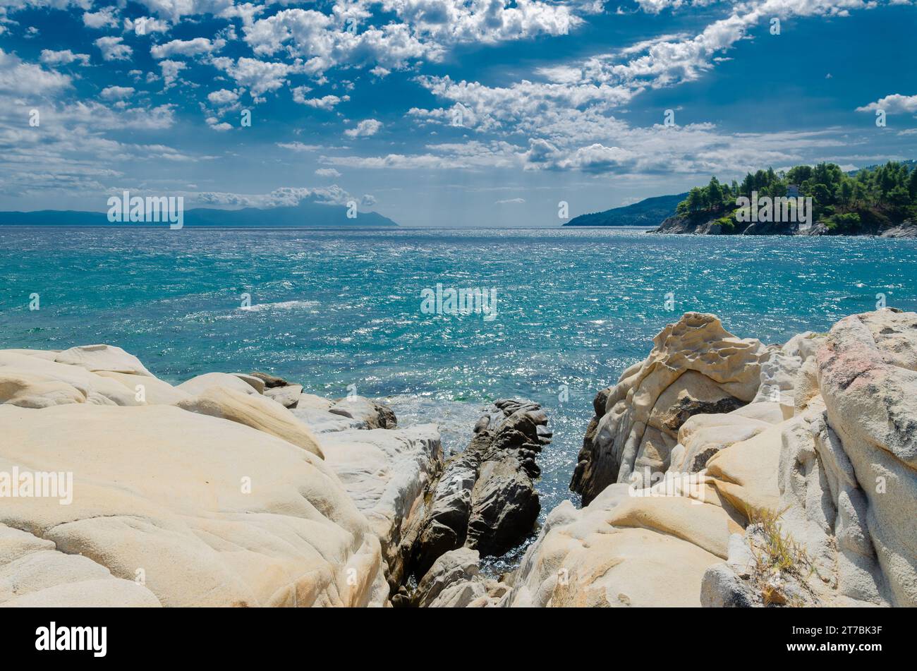 Weißer Naturmarmor in der Karidi-Lagune auf Chalkidiki. Azure Meer, im Hintergrund gegenüber der bergigen Küste einer anderen Halbinsel und Himmel mit Wolken Stockfoto