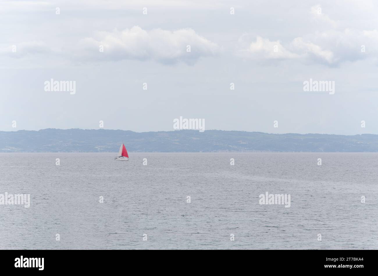 Rotes Segelboot, Küste mit Bergen, Meer und Himmel mit Wolken. Landschaft in Dunst. Hintergrund, Kopierraum Stockfoto