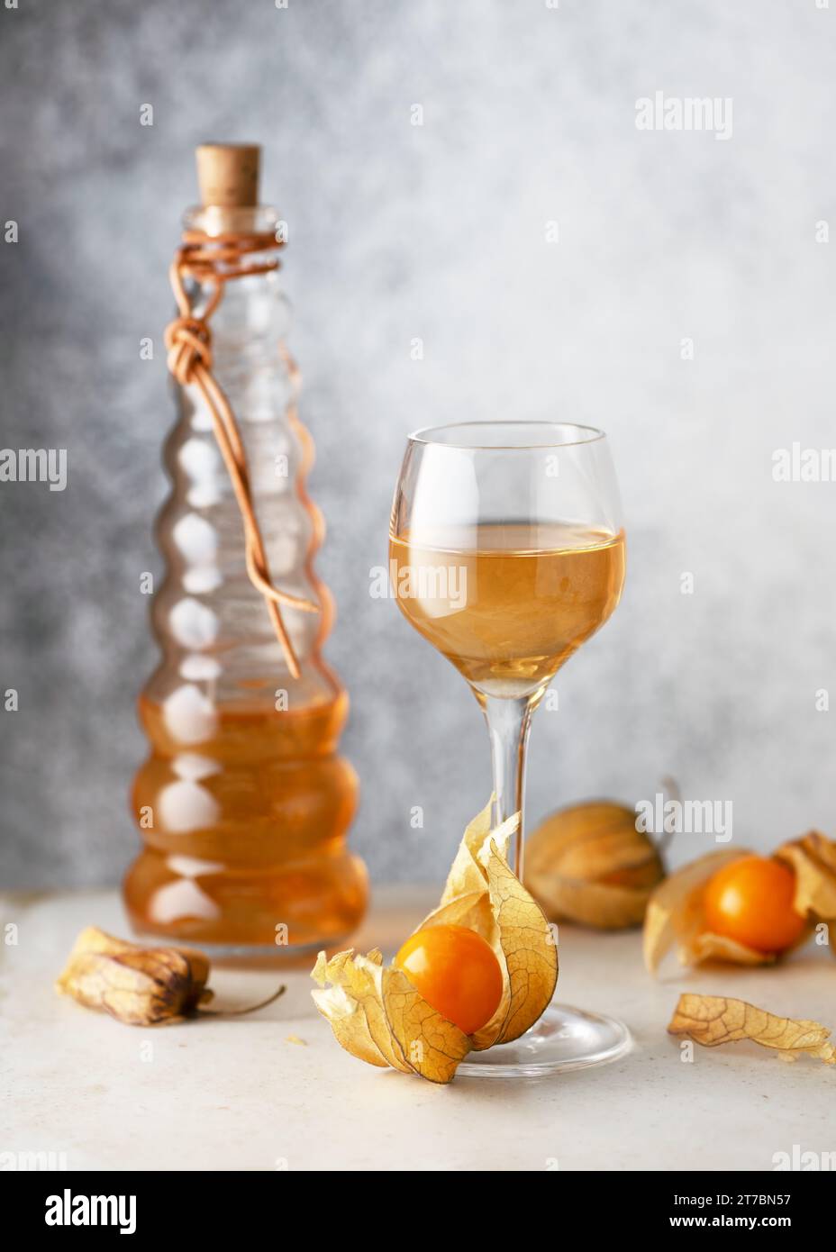 Hausgemachter Wein oder Likör von Physalis-Früchten in einem kleinen Glas mit frischen Reifen Früchten auf hellem Steinhintergrund. (Physalis pubescens) Raum kopieren. Stockfoto