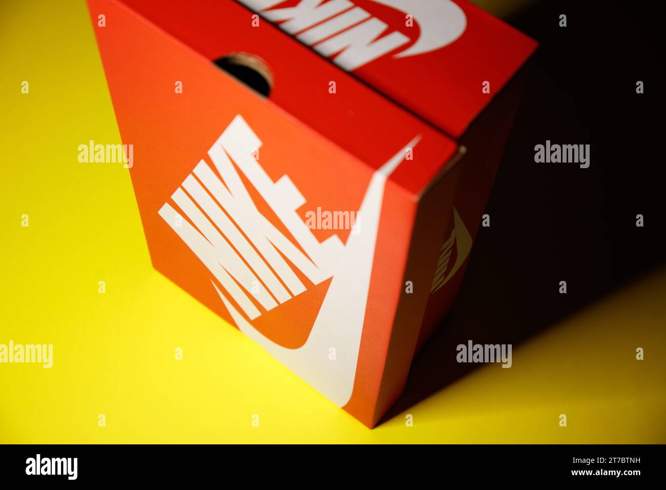 Eine originale, leuchtend rote Nike Kartonschuhbox im Vintage-Stil mit weißem Logo auf einem hellgelben Hintergrund Stockfoto