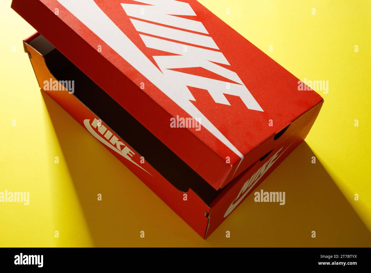 Eine originale, leuchtend rote Nike Kartonschuhbox im Vintage-Stil mit weißem Logo auf einem hellgelben Hintergrund Stockfoto