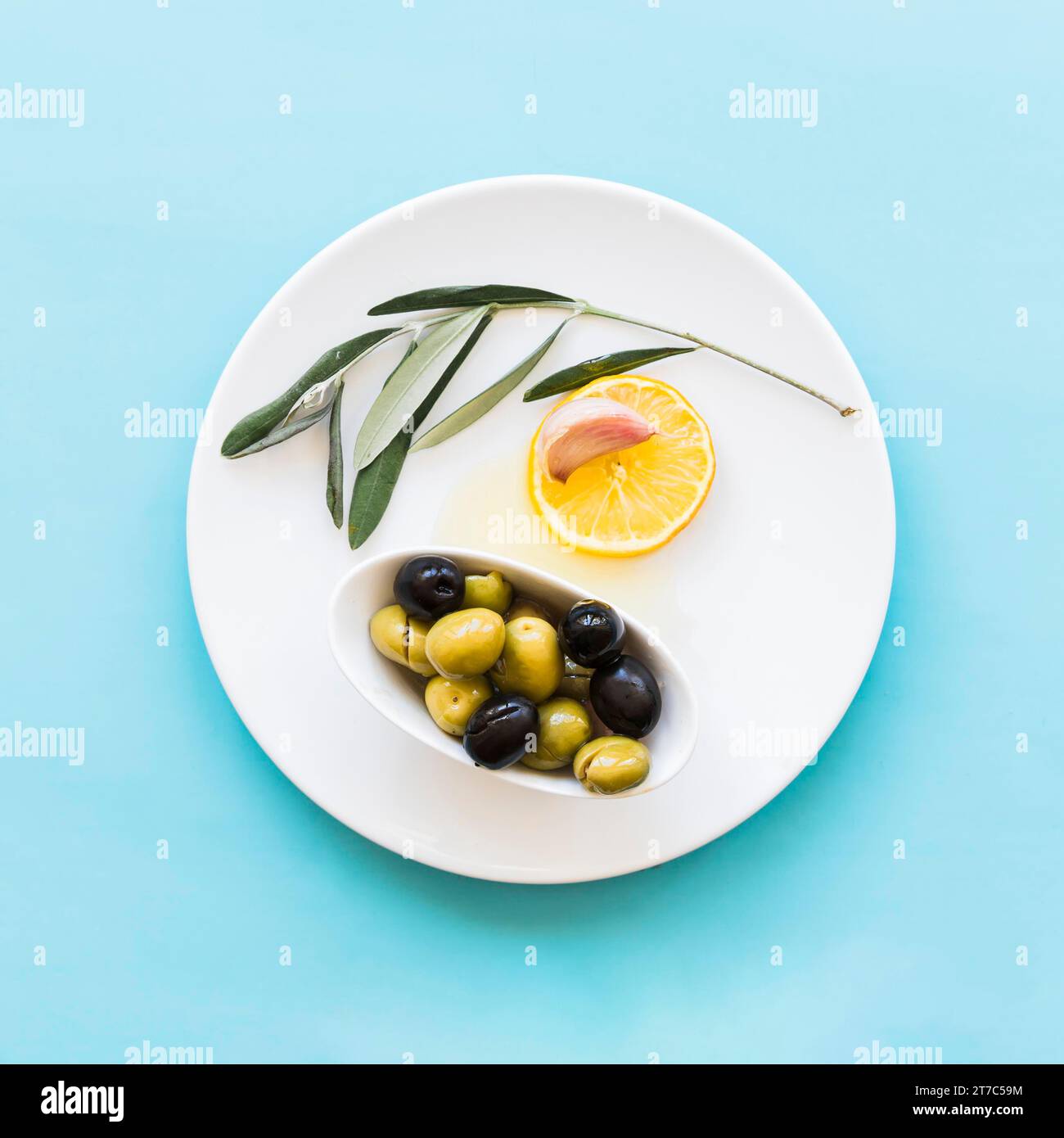 Zweig Zitronenscheibe Knoblauch Nelke Schüssel Oliven Teller blauer Hintergrund Stockfoto