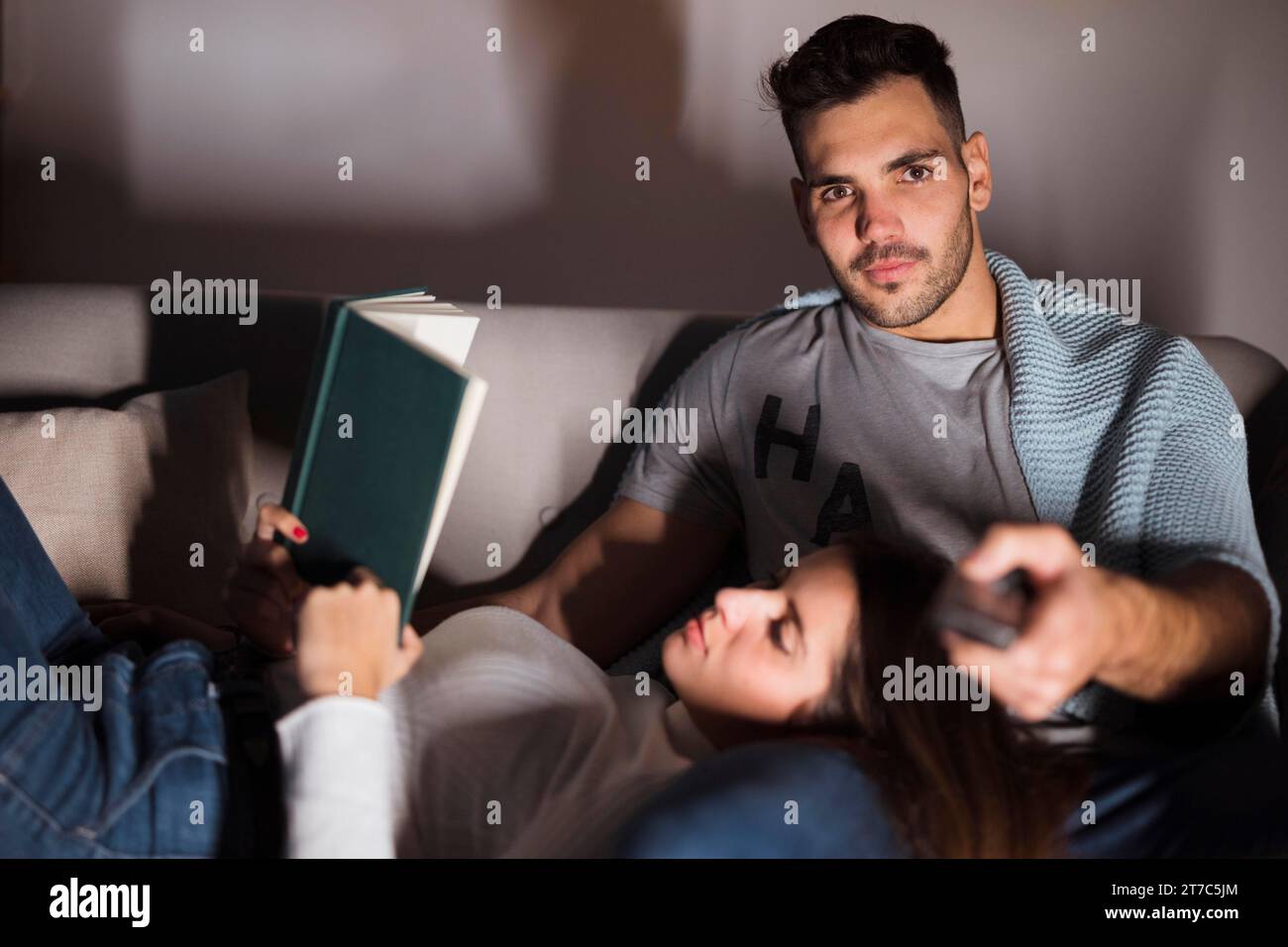 Junger Mann mit Fernbedienung Frau mit Buchsofa Stockfoto