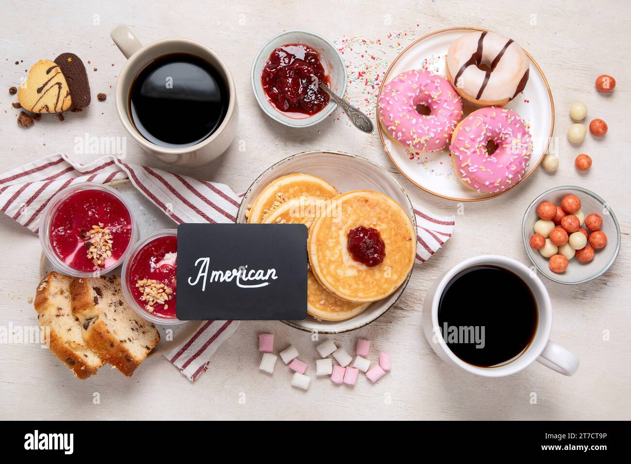 Tisch mit verschiedenen amerikanischen Keksen, Donuts, Pfannkuchen und Kaffeetassen auf weißem Hintergrund. Draufsicht. Stockfoto