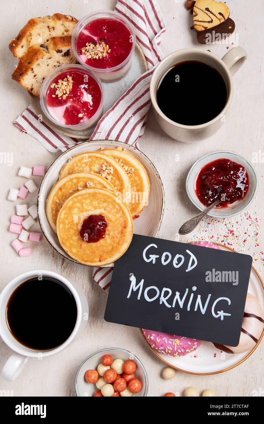 Tisch mit verschiedenen amerikanischen Keksen, Donuts, Pfannkuchen und Kaffeetassen auf weißem Hintergrund. Draufsicht. Stockfoto