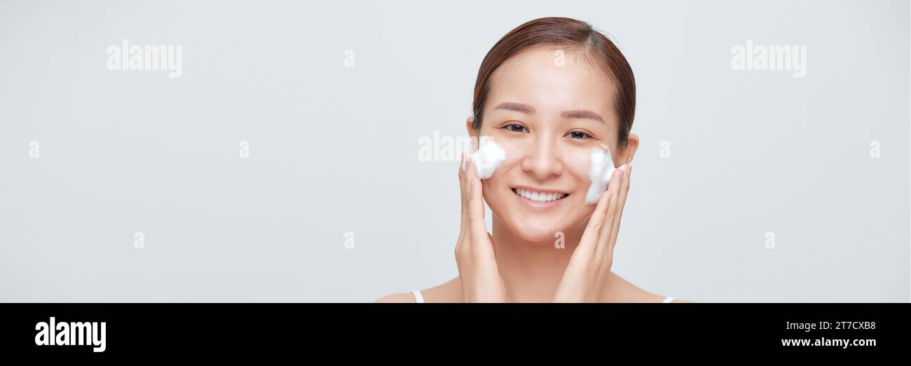 Glückliche lachende junge asiatische Frau, die Gesicht mit Schaumseife Kosmetikprodukt wäscht. Webbanner Stockfoto