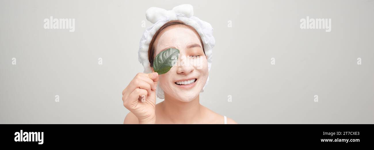 Banner der hübschen Frau hält grünes Blatt, schaut nachdenklich zur Seite, bringt Tonmaske auf das Gesicht, Stockfoto