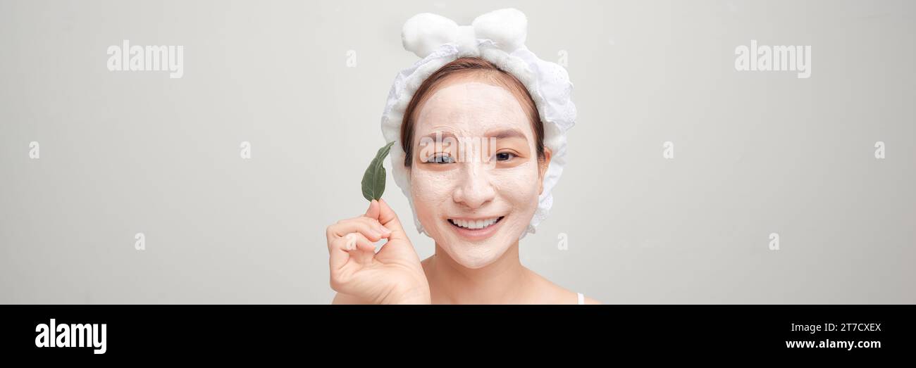 Eine Frau mit einer Tonmaske im Gesicht hält ein grünes Blatt. Panorama Stockfoto