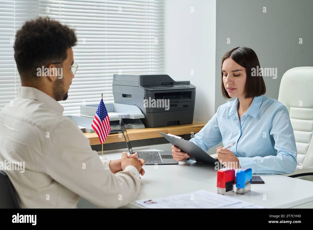 Junger Mann, der ein Interview mit einem Visumdienstmitarbeiter hat, um ein Visum zu bekommen Stockfoto