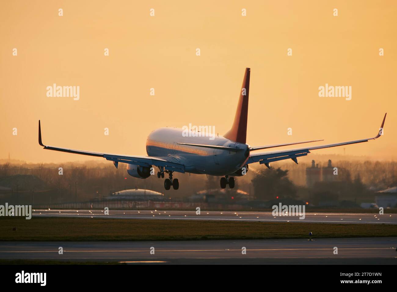 Flugzeug nähert sich der Landung auf der Start- und Landebahn des Flughafens. Passagierflugzeug im goldenen Licht des Sonnenuntergangs. Orangefarbener Himmel mit Kopierraum. Stockfoto