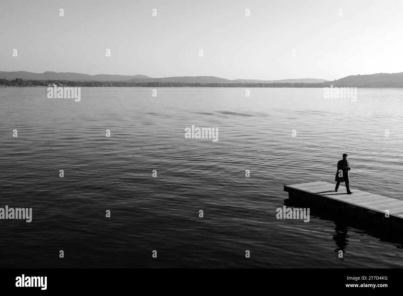 Ein Mann steht am Rande eines Piers und blickt auf ein ruhiges Wasser. Stockfoto