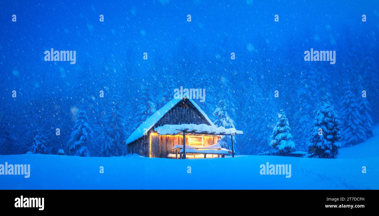 Einsame Berghütte versteckt in einer verschneiten bewaldeten Wiese mit immergrünen Bäumen im Winter. Weihnachtspostkarte. Verschneite Bergwälder Stockfoto
